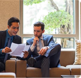Two business colleagues review a printed report together on an office sofa